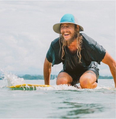 men with a surf hat paddling on a surfboard